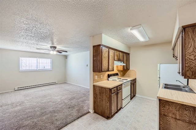 Open-concept kitchen with wooden cabinets and white appliances beside a carpeted living area.