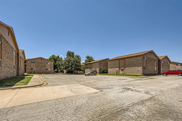 Exterior view of apartment buildings with a parking lot and trees.