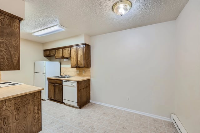 Kitchen with white refrigerator, dishwasher, and wooden cabinets.