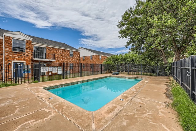 Outdoor swimming pool with concrete deck and brick buildings in background.