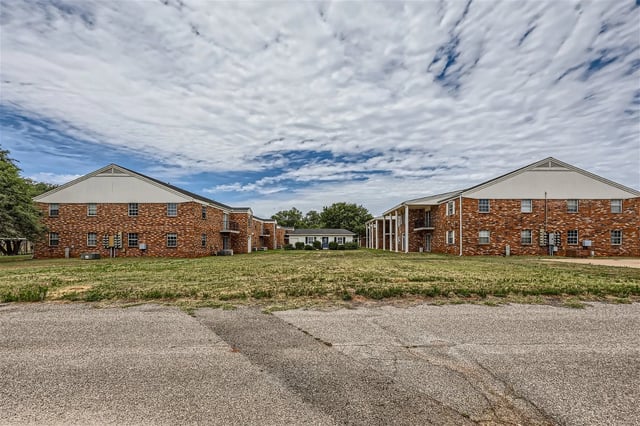 Exterior view of brick apartment buildings with a central white house and white clouds in the sky.