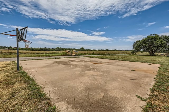 Outdoor basketball court with a hoop and backboard on a sunny day.