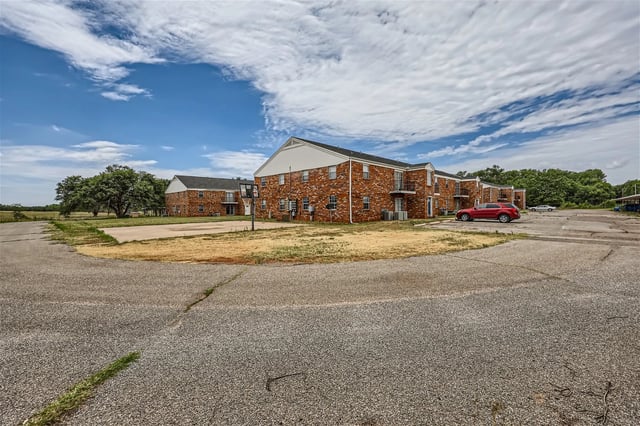 Exterior view of brick apartment buildings with a basketball hoop and parking lot.