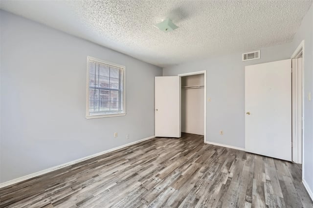 Empty bedroom with light grey walls, wood-look flooring, and a closet.