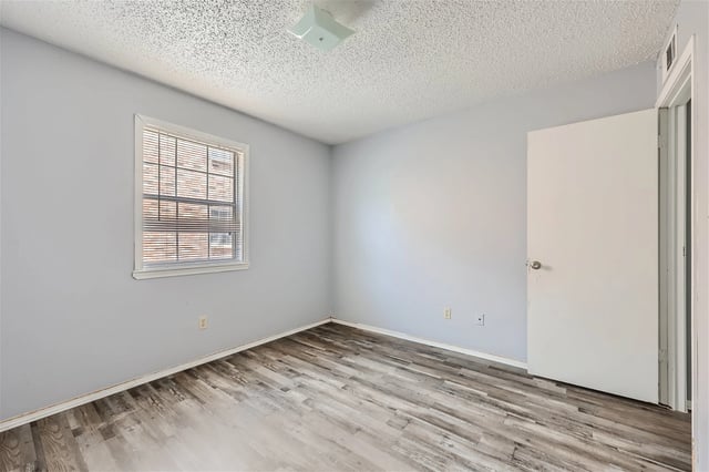 Empty bedroom with light blue walls, blinds on the window, and wood-look flooring.