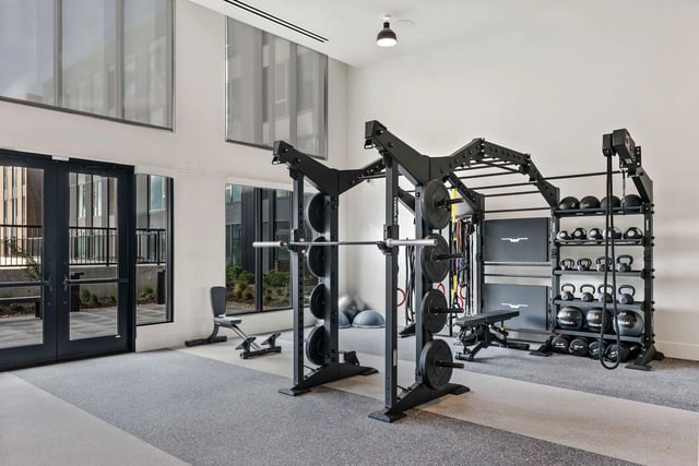 Inside a modern community gym with weight racks, barbells, and kettlebells.