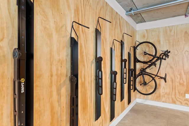 Bike storage area with multiple wall-mounted racks on a plywood wall and a bicycle.