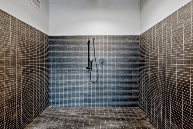 Shower area with dark gray tile walls and a handheld shower.