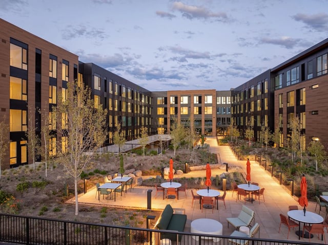 Evening view of a modern apartment courtyard with seating and orange umbrellas.