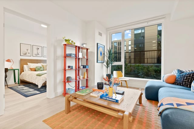 Bright living room with blue sofa, wooden coffee table, and a large window.