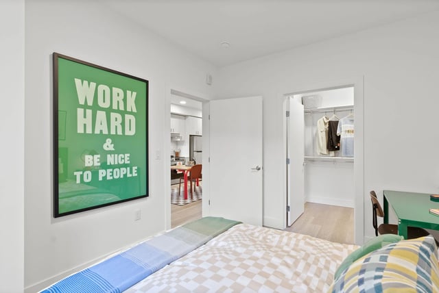 Bedroom with bed, large green art, open closet, and doorway to kitchen.