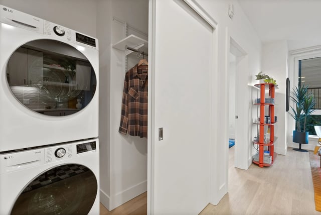 Stacked washer and dryer in a laundry alcove beside a closet and hallway.