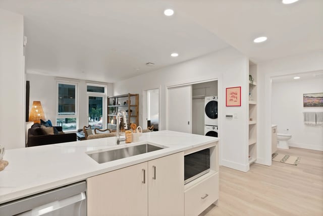 Open-concept kitchen with island and sink; living area visible, plus a laundry closet with stacked washer/dryer.