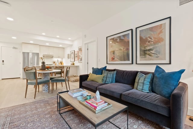 Living room in a modern apartment with a dark sofa, coffee table, and open kitchen.