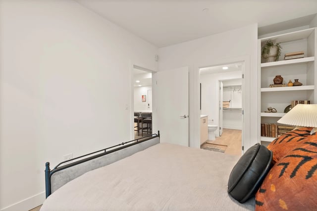 Bedroom with white walls, bed in foreground, and doors to bathroom and walk-in closet.