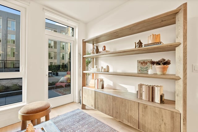 Bright living area with large window and glass door, featuring a tall wooden bookshelf.