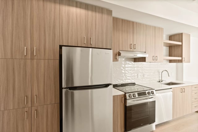 Modern kitchen with wood-tone cabinets, stainless steel refrigerator, range, and sink.