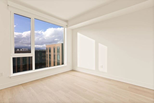 Bright empty room with large window and light wood floors.