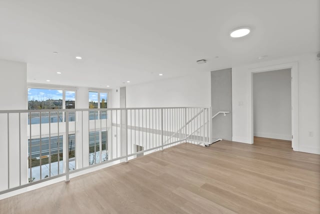 Upper-floor loft-style apartment interior with white railing, large windows and light wood flooring.