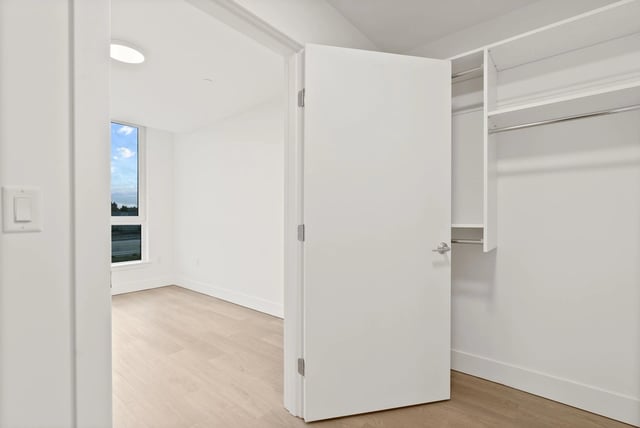 Open white walk-in closet with shelves and rod, opening to a bright room with a window.