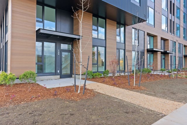 Exterior entrance of a modern apartment building with glass doors and landscaped walkway.