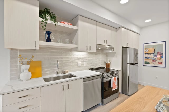 Modern apartment kitchen with light wood cabinets and stainless steel appliances.