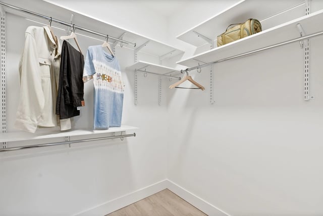 Walk-in closet with white walls, hanging rods, shelves, and clothing on hangers