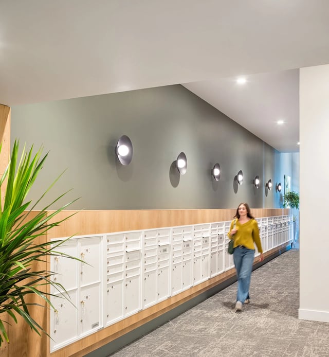 Person walking down a hallway with a long row of white mailboxes and modern wall lights.