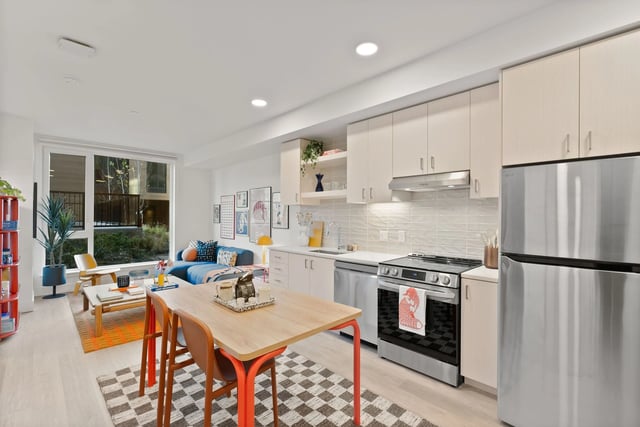 Open-concept kitchen and living area in a modern apartment with light cabinets and stainless steel appliances.
