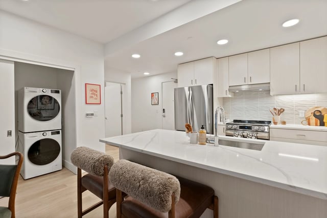 Modern kitchen with island, stainless appliances, and a stacked washer/dryer in a closet.