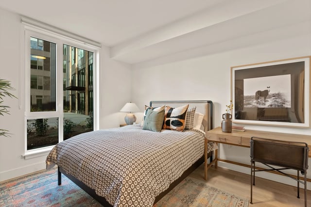 Bedroom in an apartment with a bed, desk, and a large window.
