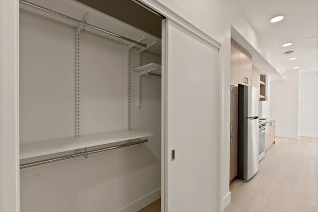 Open closet with shelves and rods next to a modern kitchen with stainless fridge.