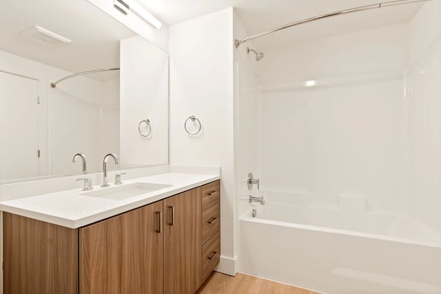 Bathroom with a double vanity, wood cabinets, large mirror, and a bathtub with shower.