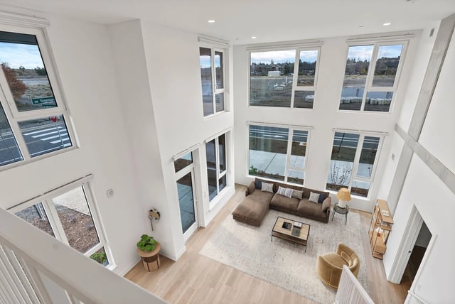 Bright two-story living room with large floor-to-ceiling windows and a sectional sofa.