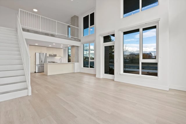 Bright open-concept living area with a two-story ceiling, large windows, and an island kitchen.