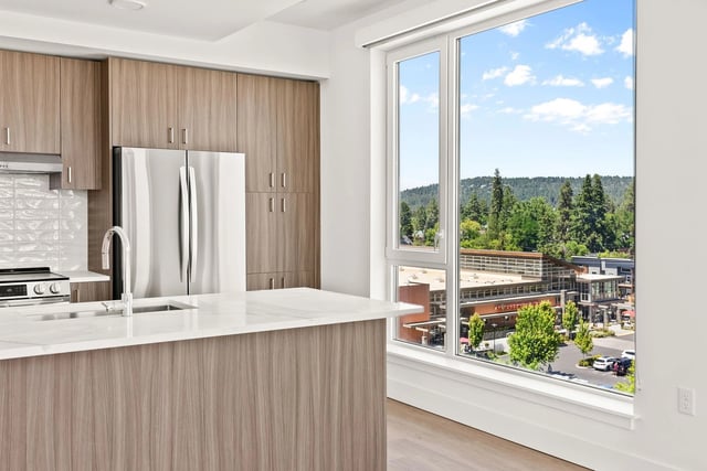 Modern kitchen with wood-tone cabinets, stainless steel appliances, and a large window with outdoor view.