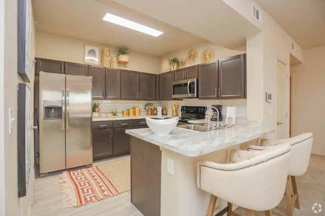 Modern kitchen with stainless steel appliances, dark wood cabinets, and marble countertops.