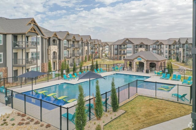 Outdoor swimming pool with lounge chairs and a covered seating area at a modern apartment complex.