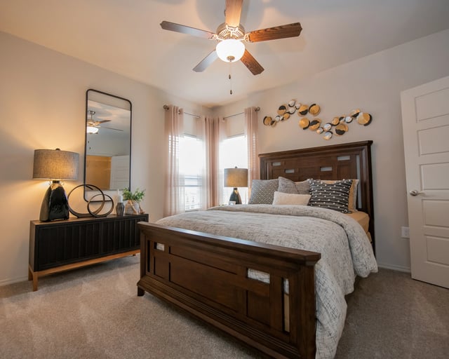 A bedroom with a large bed, a ceiling fan, and a mirror.