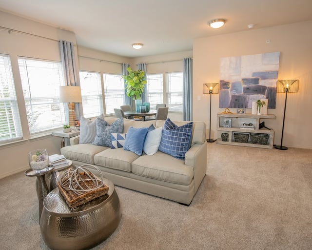 A living room with a beige couch, a round table with a basket on it, and a large painting on the wall.
