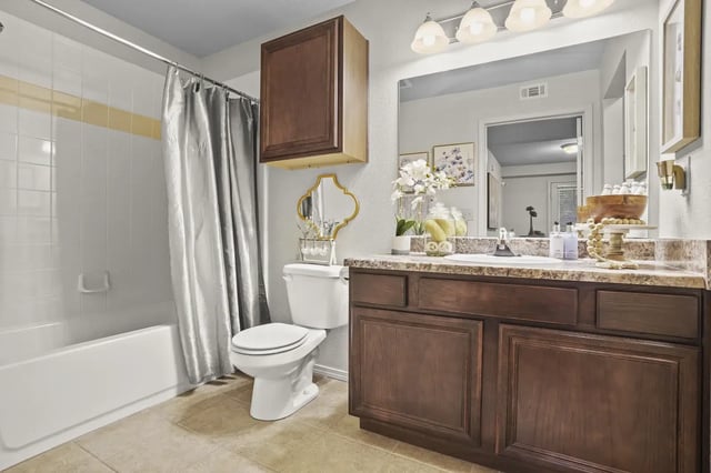 Apartment bathroom with a wooden vanity, mirror, toilet, and shower-tub with a gray curtain.