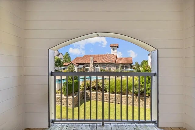 View from a balcony opening onto a landscaped community courtyard with a pool and red-tiled buildings.