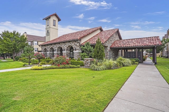Building exterior with arched stone entryway and tower, surrounded by manicured lawns and landscaping.