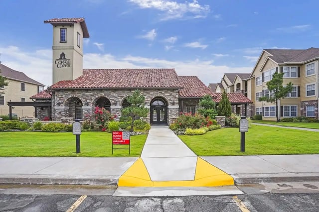 Exterior view of a stone-clad clubhouse with a red-tile roof and landscaped entrance at an apartment community.