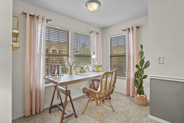 Desk with chair in a room with large windows, pink curtains, and a tall potted cactus.