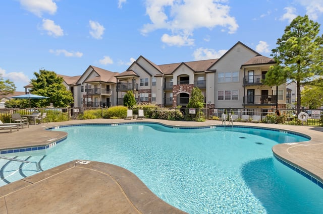 Outdoor swimming pool with lounge chairs and apartment buildings in the background.