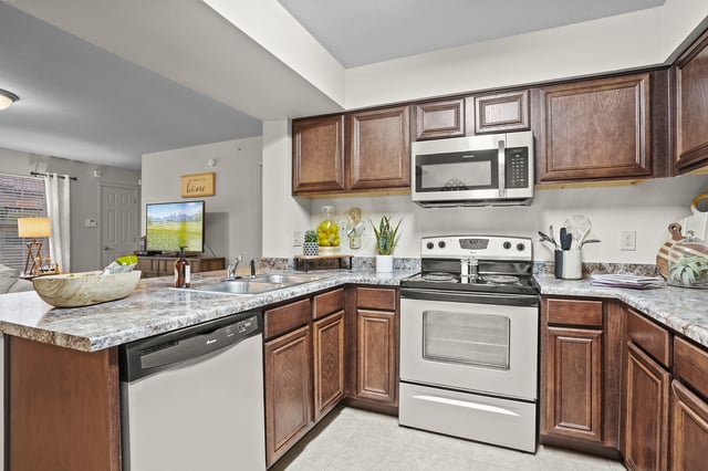 Modern kitchen with dark wood cabinets, granite countertops, stainless steel microwave, and white stove.