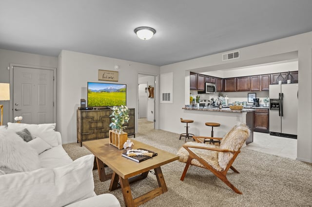 Living room and kitchen of an apartment, featuring a sofa, coffee table, TV, and bar stools.