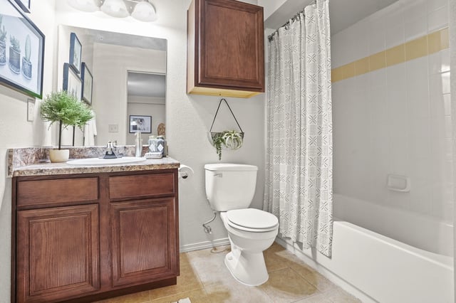 Modern apartment bathroom with wood vanity, sink, toilet, and bathtub with shower curtain.