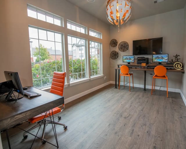 Bright apartment home office with a long desk, orange chairs, and large windows.